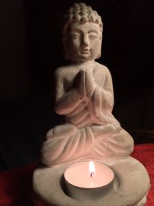 Betender Buddha aus Stein, mit einem brennenden Teelicht auf dem Schoß. Praying Buddha made of stone with a burning tea light on the lap.